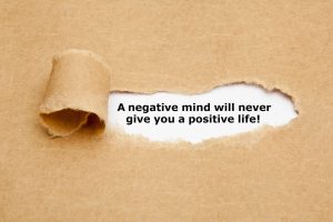 The text A negative mind will never give you a positive life, appearing behind torn brown paper.